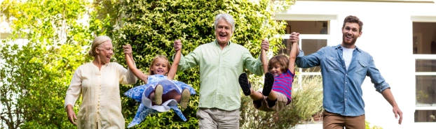 Two grandparents, a father, and two kids playing on the grass in their front yard.