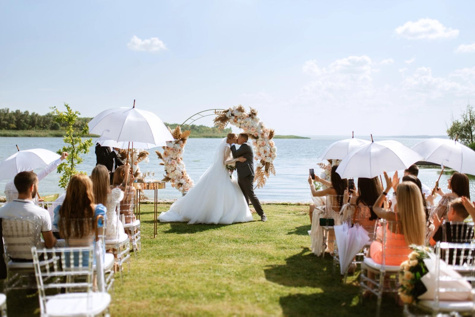 An outdoor wedding ceremony in a grassy area beside a lake.