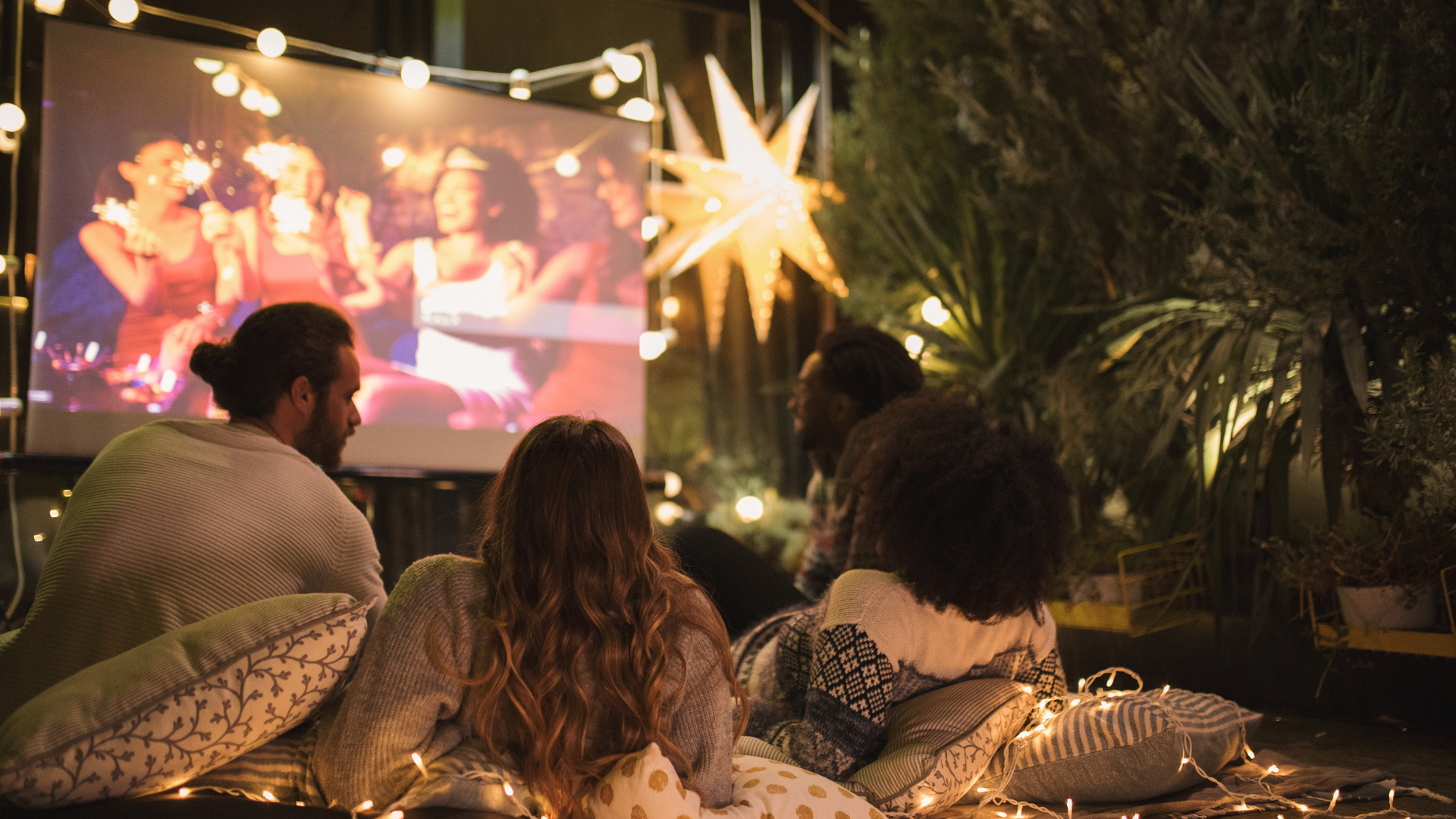 A group of friends watching a movie on a projector screen in their backyard.